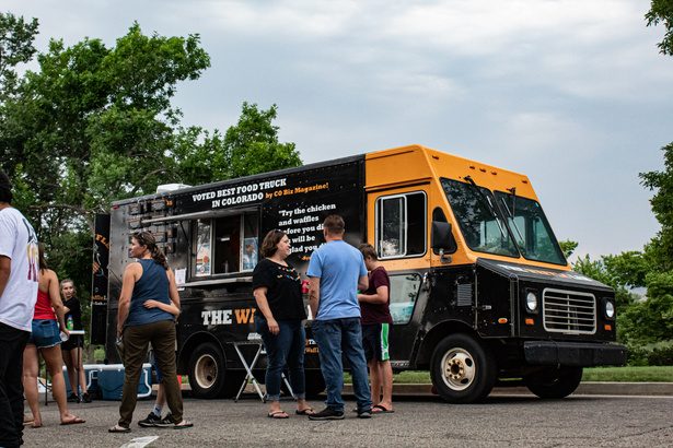 Neighbors gathered around a food truck under big trees near City Park in Fort Collins