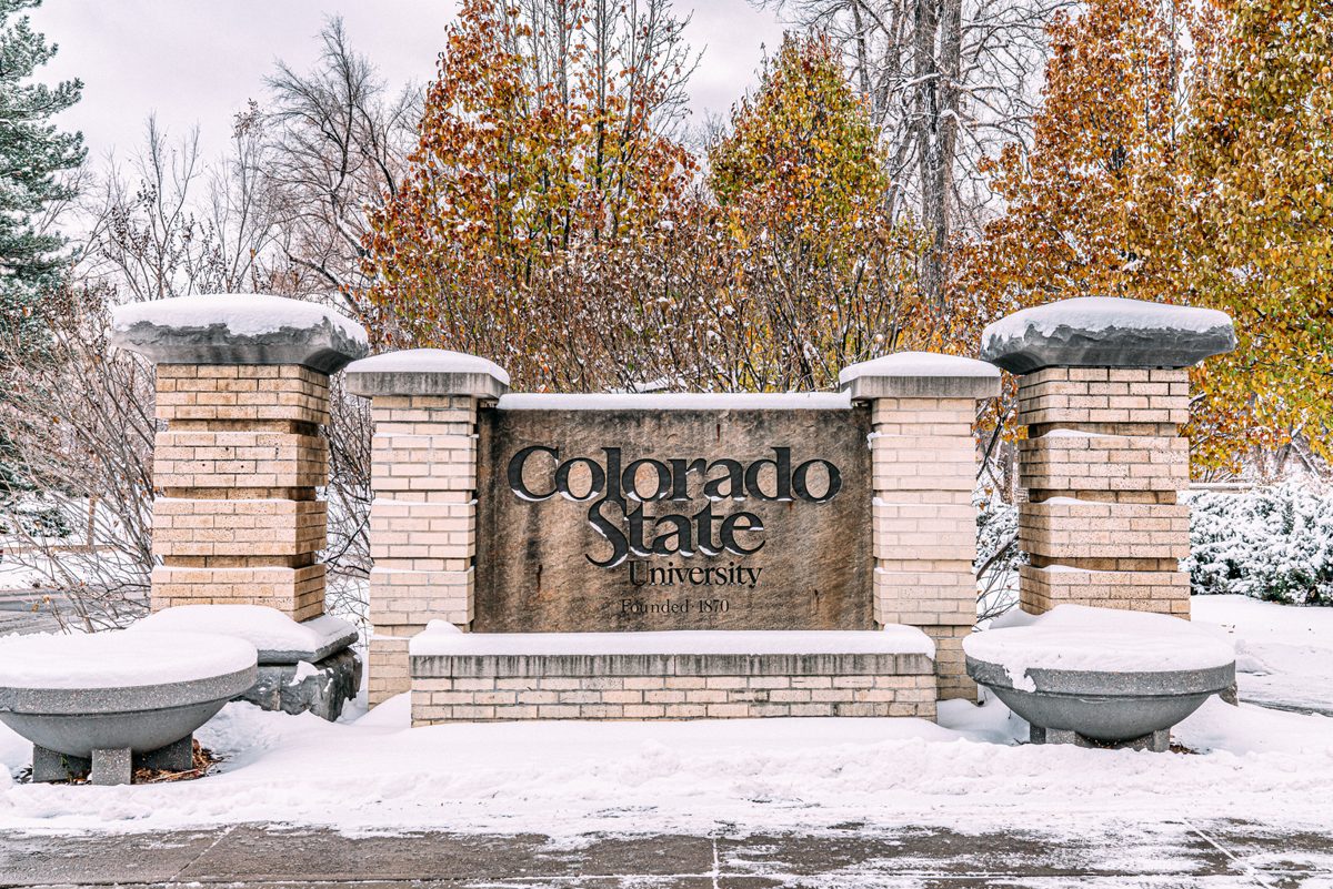 Snow-covered Colorado State University entrance sign with fall trees in Fort Collins